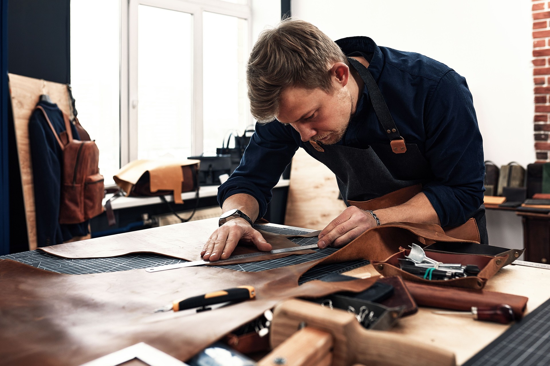 leather craftsmen working making measupenets in patterns at table in workshop studio